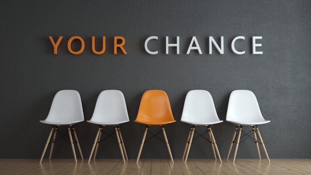 Vier weiße Stühle und ein Stuhl in Orange mit dem Spruch an der Wand Your Chance