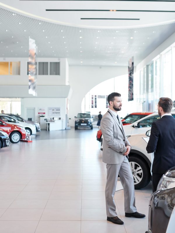 Professional salesperson selling new cars in a modern auto salon. Two men standing and choosing a new car